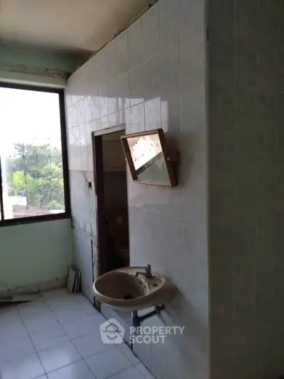 Spacious bathroom with large window and wall-mounted sink, offering potential for renovation.