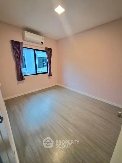 Spacious bedroom with wooden flooring and large window, perfect for natural light.