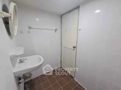 Compact bathroom with white tiles and brown floor, featuring a sink and mirror.