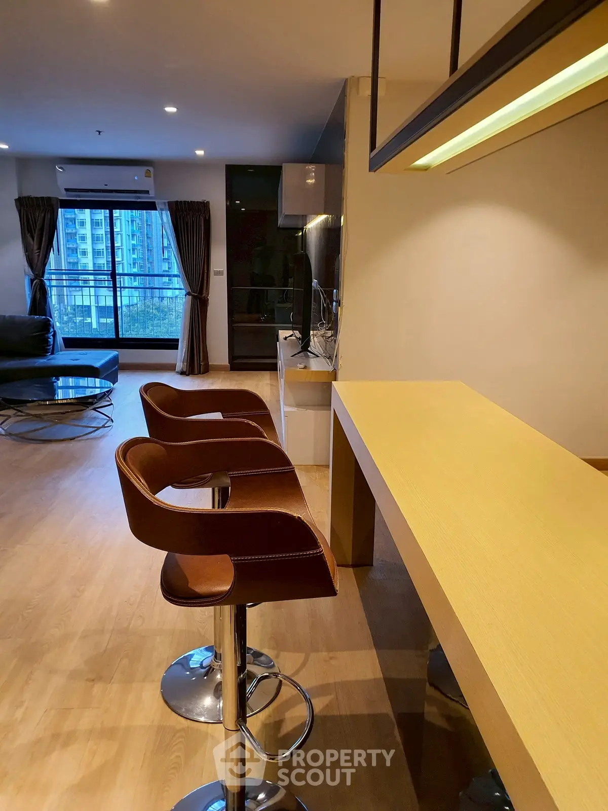 Modern living room with stylish bar stools and large windows offering city views.
