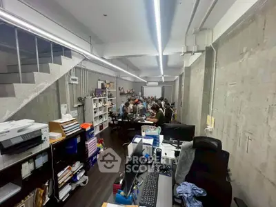 Modern office space with open layout and industrial design, featuring desks, shelves, and a staircase.