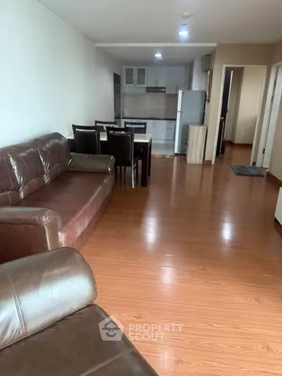 Spacious living room with leather sofa and dining area leading to modern kitchen.