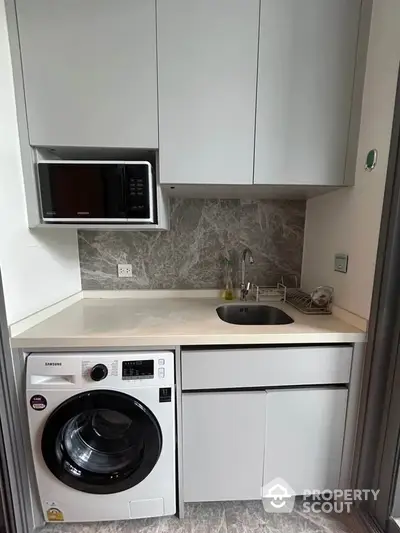 Modern compact laundry area with washing machine and microwave in sleek cabinetry.