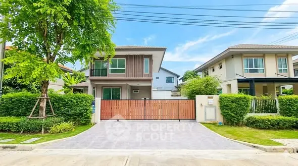 Modern two-story house with lush greenery and gated driveway in a suburban neighborhood.