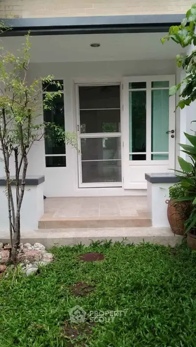 Charming house entrance with lush garden and modern glass door, perfect for welcoming guests.