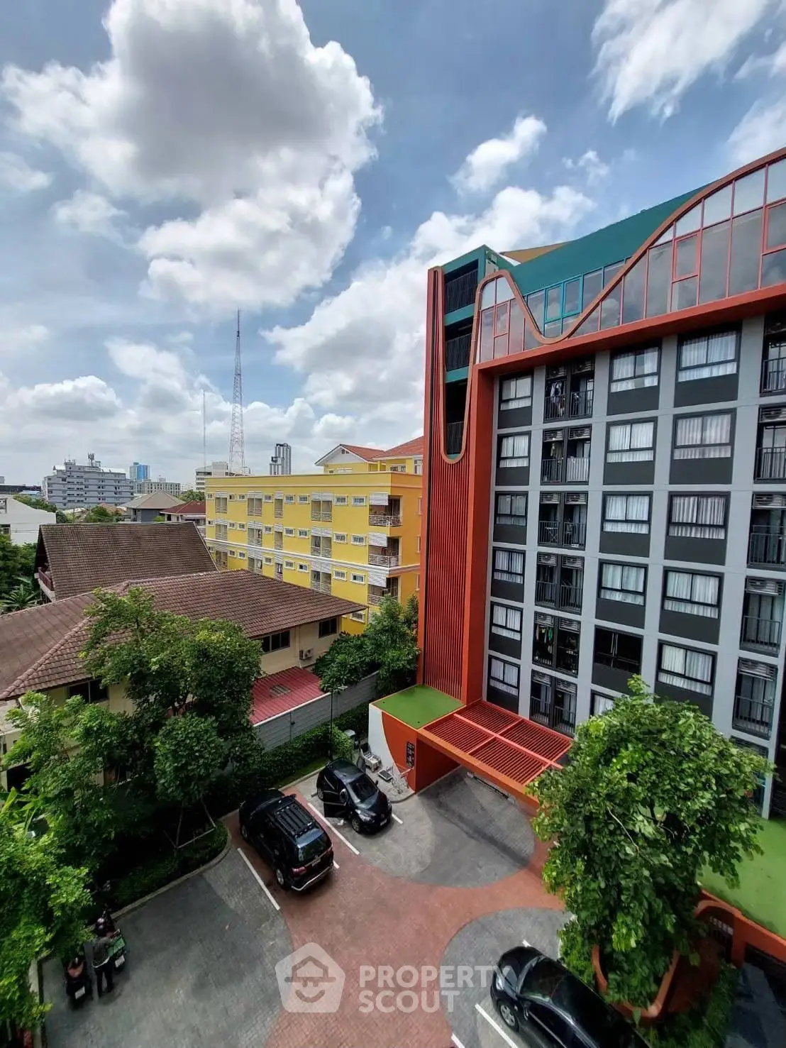 Modern apartment building with vibrant colors and spacious parking area under a clear sky.