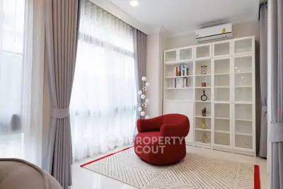 Elegant living room with modern red chair, large windows, and stylish shelving unit.