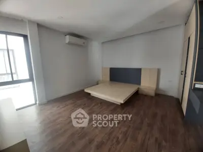 Spacious bedroom with modern wooden flooring and built-in air conditioning unit.