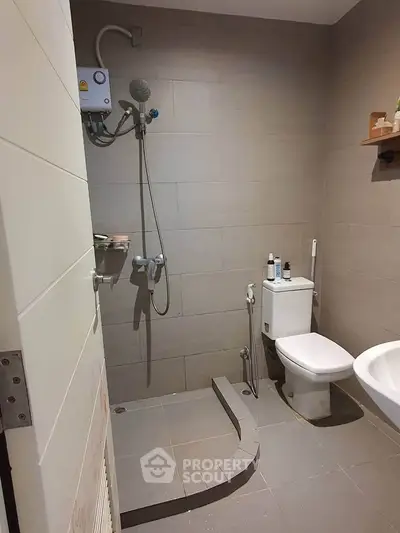 Modern bathroom with shower and toilet in minimalist design, featuring neutral tiles and compact layout.