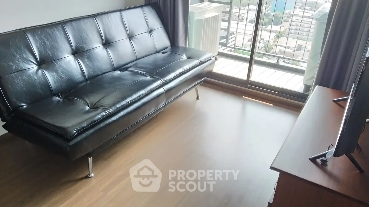 Modern living room with sleek black leather sofa and balcony view, perfect for urban living.