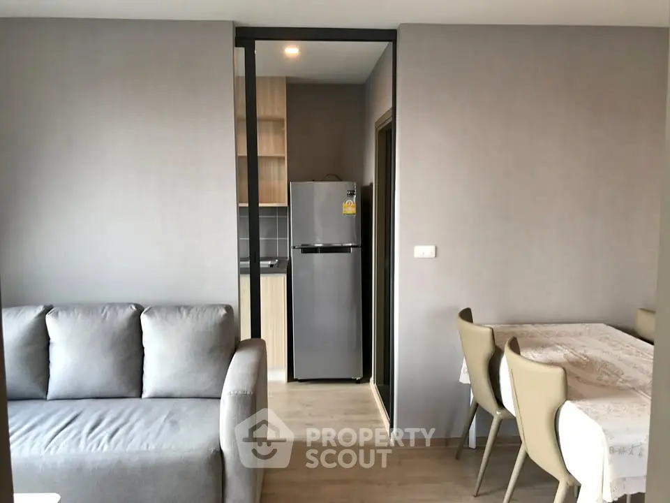 Modern apartment interior with cozy living room and dining area, featuring a sleek kitchen with stainless steel fridge.