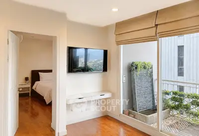 Modern bedroom with balcony access and wall-mounted TV, featuring wooden flooring and natural light.