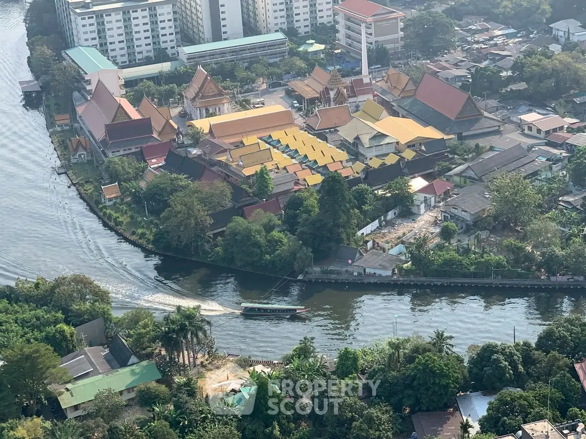 Aerial view of riverside residential area with lush greenery and traditional architecture.