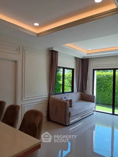 Elegant living room with modern decor and large windows overlooking lush greenery.