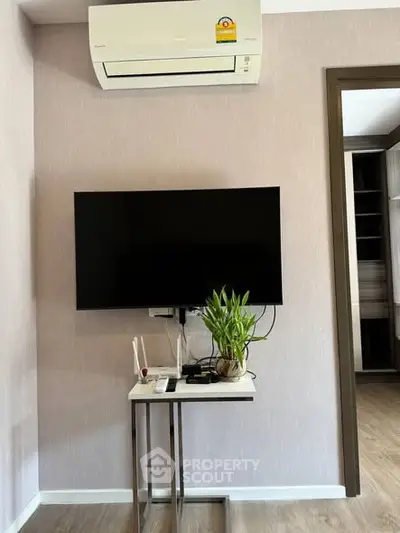 Modern living room with wall-mounted TV and air conditioning unit, featuring sleek decor and a touch of greenery.