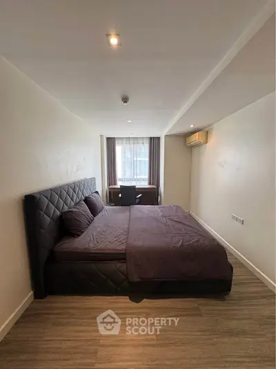 Spacious bedroom with modern decor and large window offering natural light.