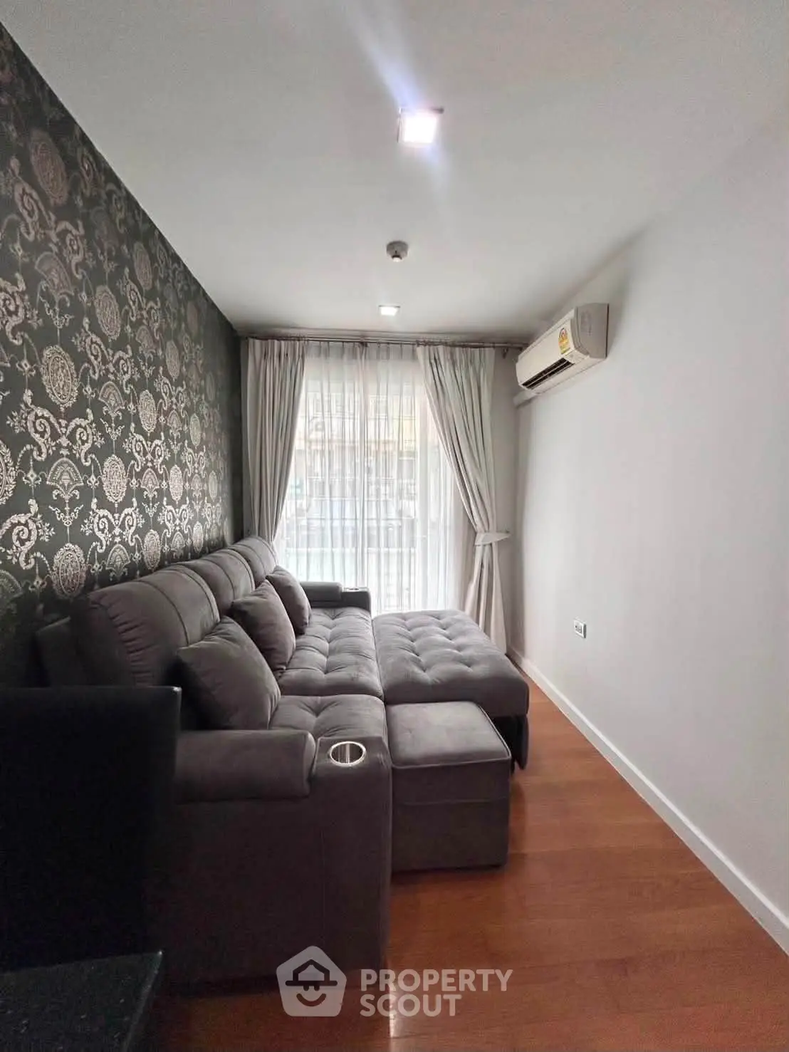 Cozy living room with elegant wallpaper and plush sectional sofa, featuring natural light from large window.