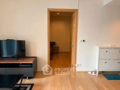 Spacious living room with modern TV setup and wooden flooring, leading to a cozy interior space.