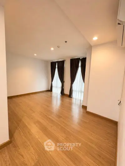 Spacious empty room with wooden flooring and large windows, perfect for customization.