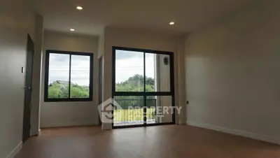 Spacious empty room with large windows and wooden flooring, offering serene green views.