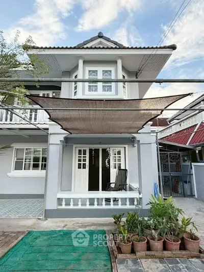 Charming two-story house with a welcoming front porch and lush potted plants, perfect for family living.