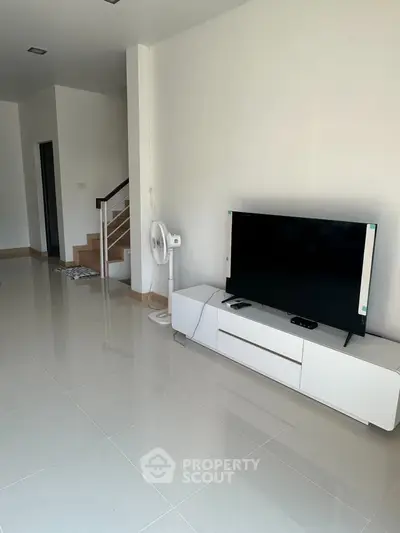 Modern living room with sleek TV stand and staircase, featuring glossy tile flooring and minimalist decor.