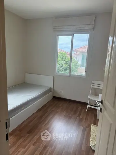 Cozy bedroom with wooden flooring and natural light from window.