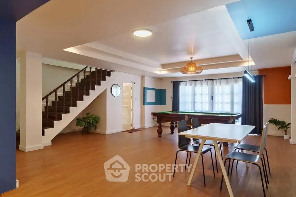 Spacious modern living room with pool table and dining area, featuring stylish lighting and wooden flooring.