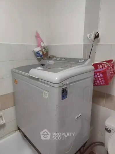 Compact bathroom with washing machine and tiled walls, ideal for small spaces.