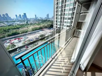 Spacious balcony with stunning city view overlooking a pool in a modern high-rise apartment.