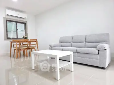 Modern living room with gray sofa, white coffee table, and dining set in bright interior.