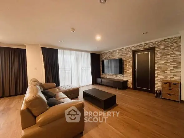 Spacious modern living room with leather sofa and wall-mounted TV, featuring elegant wood flooring and stylish decor.