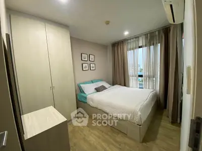Cozy bedroom with wooden flooring, large window, and modern furnishings in a stylish apartment.