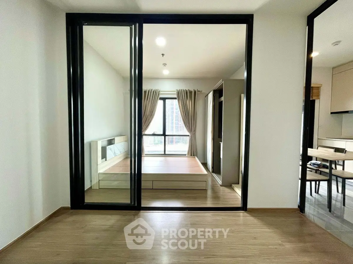 Modern bedroom with large mirror and wooden flooring, featuring a bright window view.
