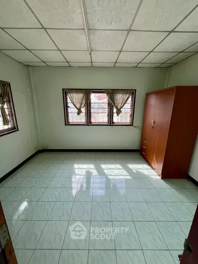 Spacious empty bedroom with tiled floor and large windows for natural light.