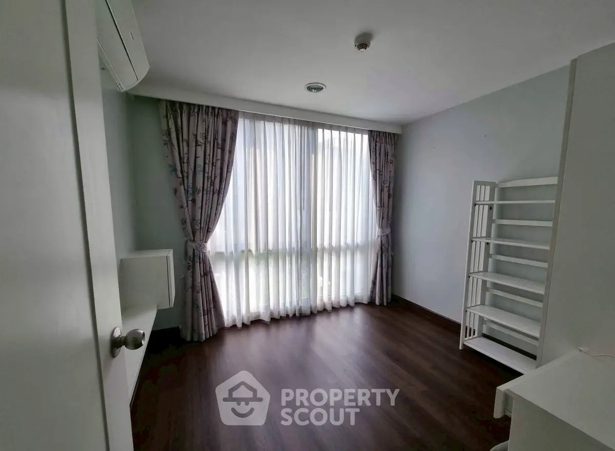 Spacious empty room with large window and wooden flooring, perfect for customization.