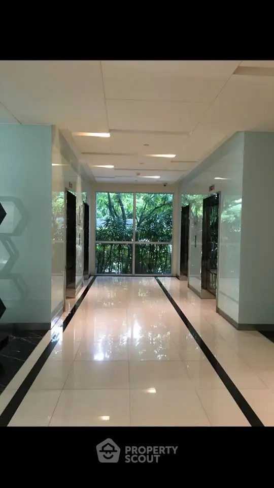 Modern building corridor with elevators and large window view of greenery.