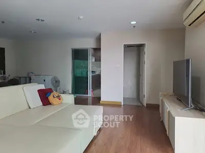 Spacious living room with modern furniture and wooden flooring, featuring a cozy sofa and large TV.