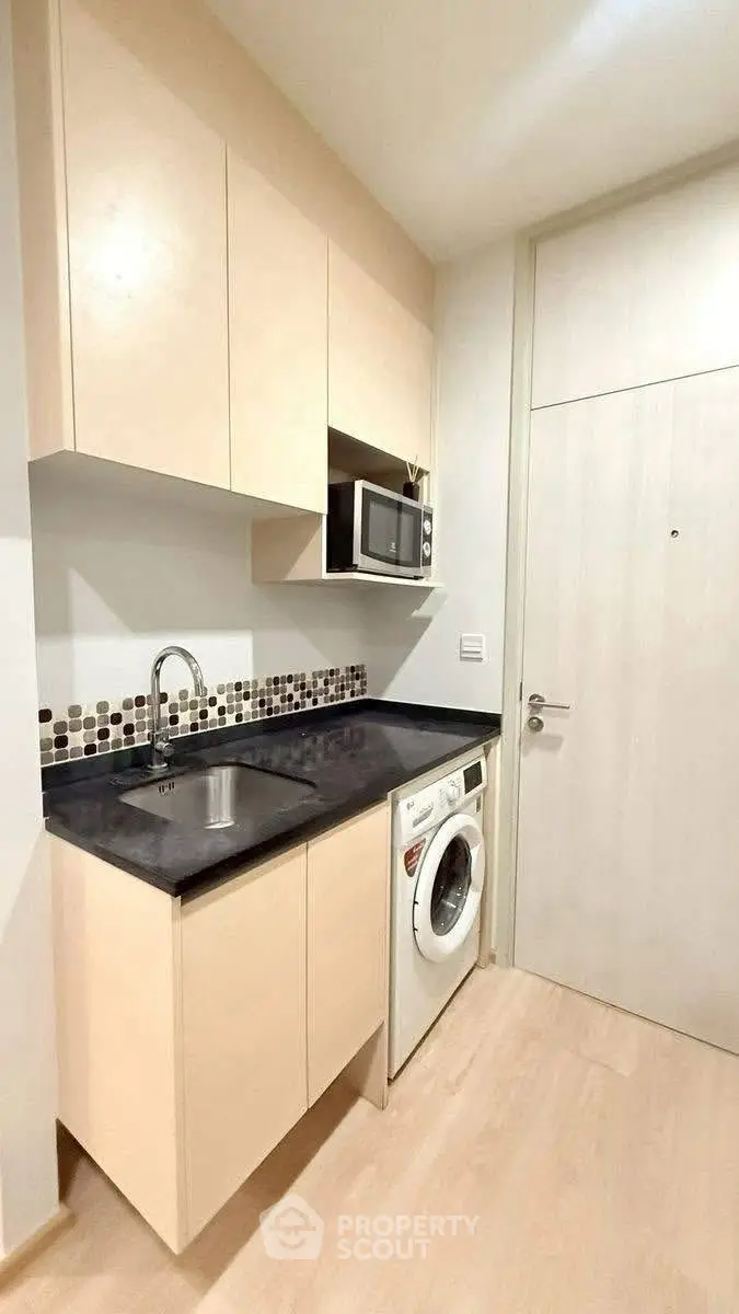 Modern compact kitchen with washing machine and microwave in sleek apartment.