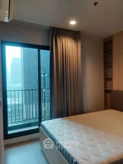 Modern bedroom with large window and city view, featuring a comfortable bed and elegant curtains.