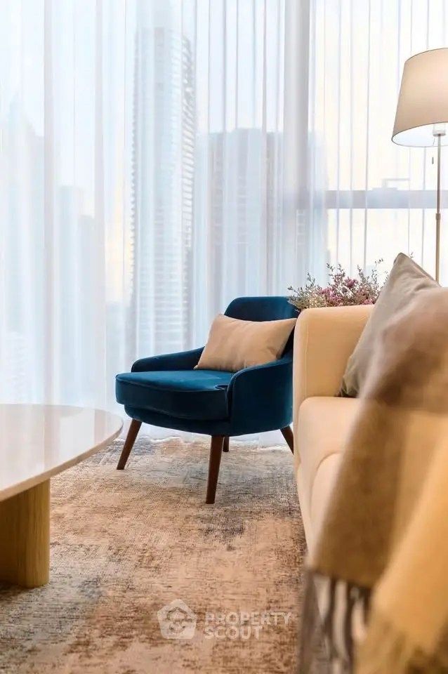 Elegant living room with plush blue armchair and modern decor, featuring floor-to-ceiling windows with city view.