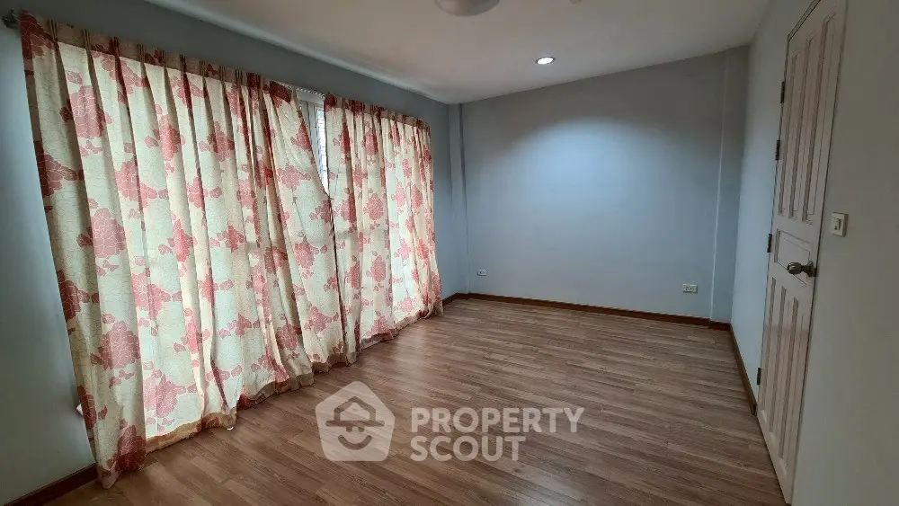Spacious empty room with wooden flooring and floral curtains, perfect for customization.
