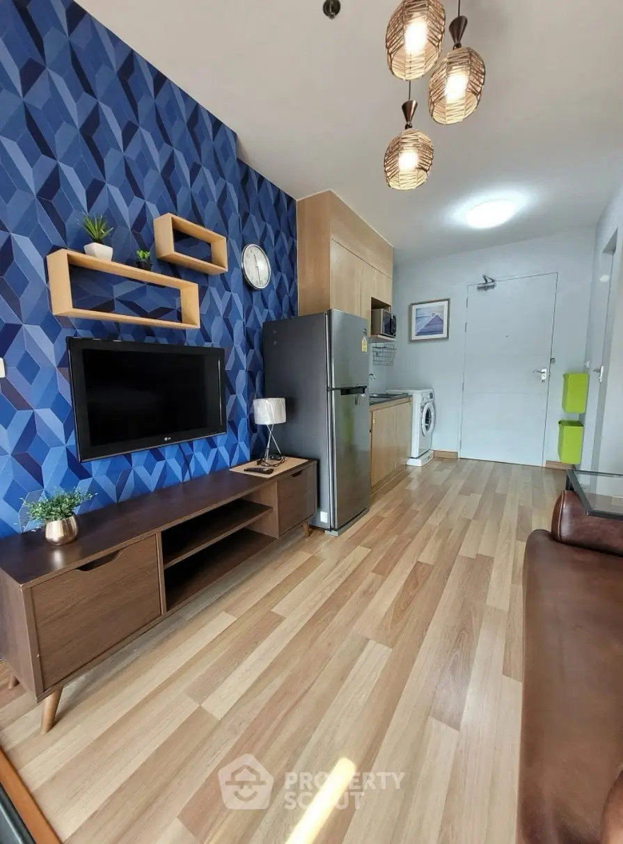 Modern living room with stylish decor, wooden flooring, and open kitchen layout featuring fridge and washing machine.