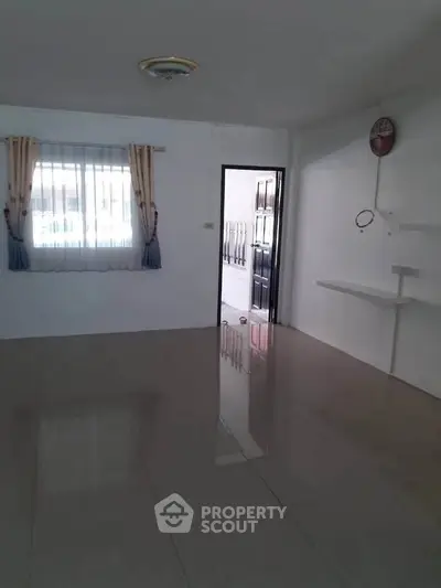 Spacious empty room with glossy tiled floor and natural light from window.