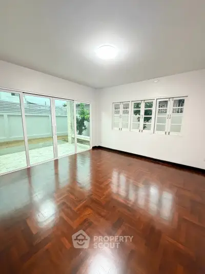 Spacious living room with wooden flooring and large windows offering natural light.