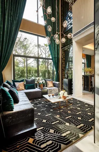 Luxurious living room with high ceilings, elegant chandelier, and large windows offering garden views.