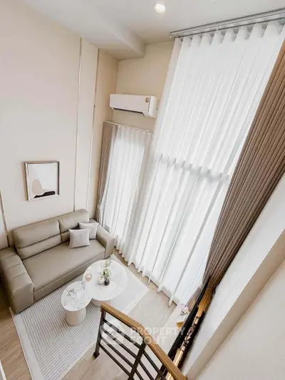 Modern living room with high ceilings and large windows, featuring a cozy sofa and elegant decor.