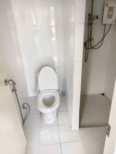 Compact bathroom with white tiles and modern fixtures, featuring a shower and toilet.
