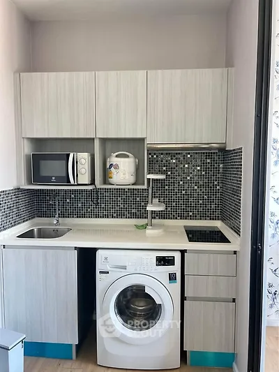 Modern compact kitchen with washing machine and microwave, sleek cabinetry and stylish backsplash.