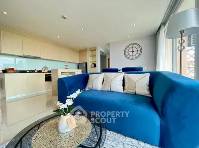 Modern living room with blue sofa and open kitchen layout, featuring stylish decor and ample natural light.